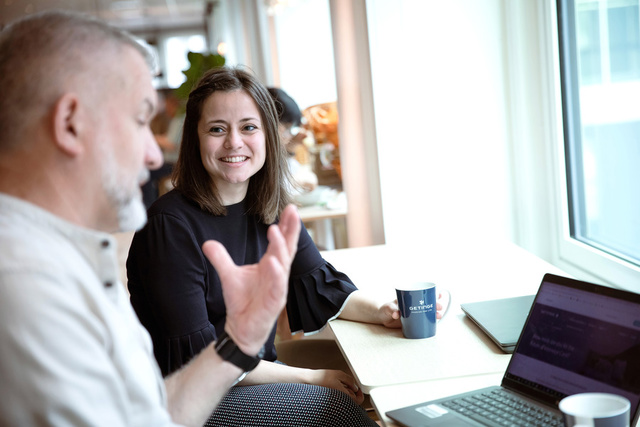Woman and man talking in an office environement in front of a window