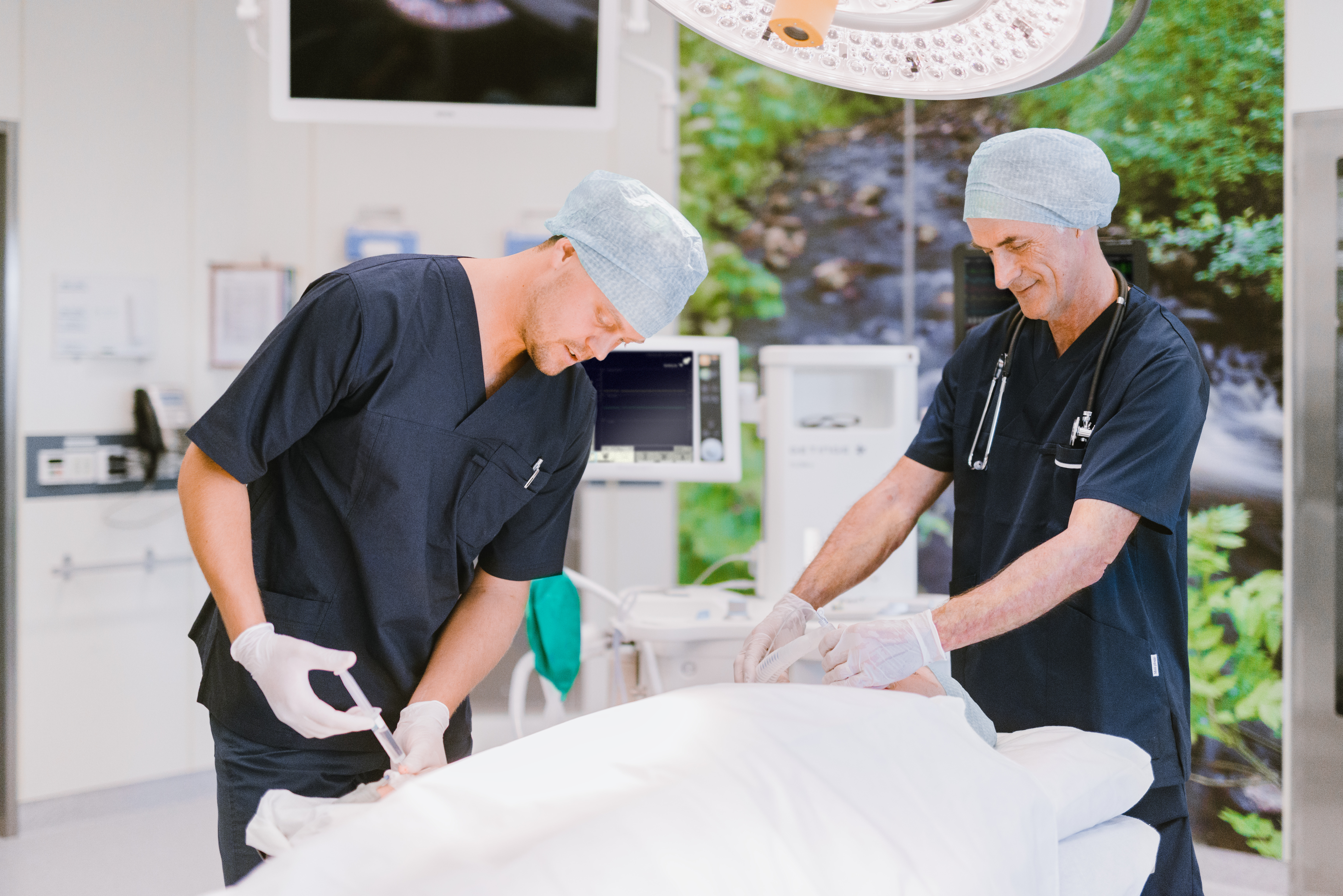 Two medical professionals in scrubs and caps tending to a patient in an operating room.