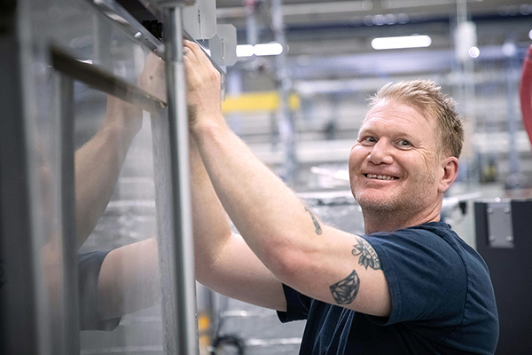 Lächelnder Mann mit Tätowierungen, der in einem industriellen Umfeld an Maschinen arbeitet.