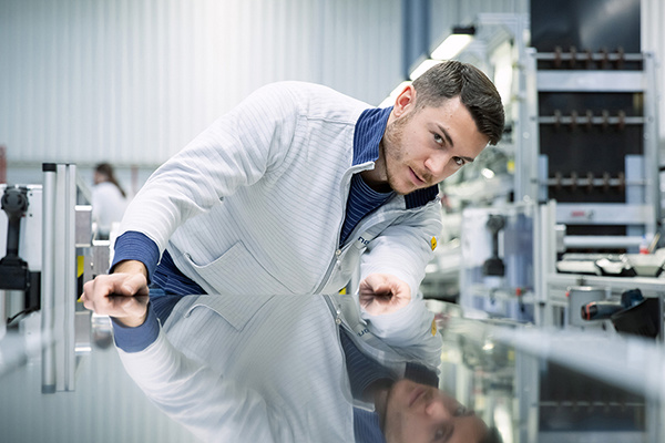 Mann im weißen Laborkittel lehnt in einer modernen Laborumgebung über einer reflektierenden Oberfläche.