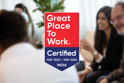 Logo reads Great Place To Work Certified May 2023 - May 2024 INDIA with blurred people conversing in the background.
