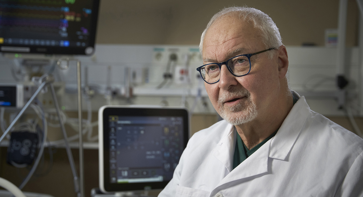 Doctor in a white coat with medical equipment and monitors in the background.
