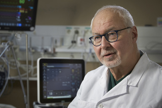 Doctor in a white coat with medical equipment and monitors in the background.