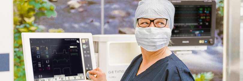 Een zorgverlener met een masker op bedient een Flow-c anesthesietoestel in de operatiekamer.