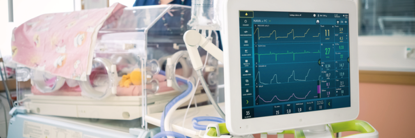 De monitor van een Servo-n beademingsmachine voor een couveuse met daarin een baby, bedekt met een roze deken.