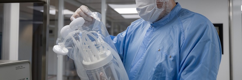 Labortechniker in blauer Schutzkleidung untersucht Geräte in einem sterilen Raum.