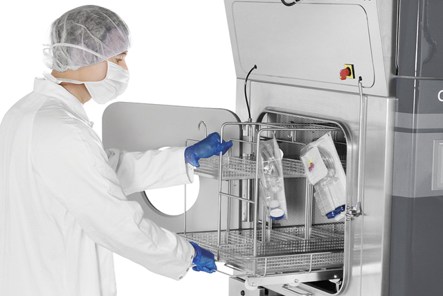 Un opérateur habillé d'une combinaison adaptée aux environnements stériles charge du matériel dans un isolateur pour biodécontamination.