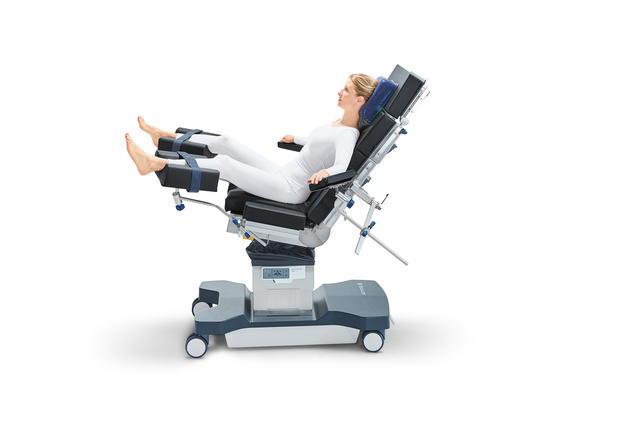 Person reclined in a motorized medical chair, feet elevated, wearing a white outfit.
