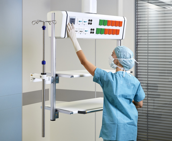 A medical professional adjusts equipment in a hospital room with an IV stand and control panel.