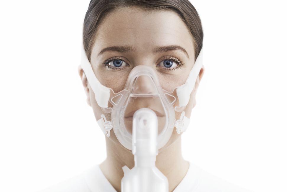 A woman wearing a clear oxygen mask with a white background.