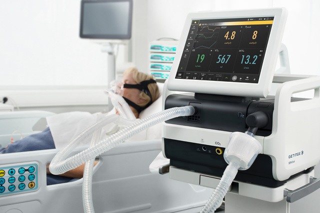 Adult patient in hospital bed wearing non-invasive mask and ww5 Servo-air co2 mechanical ventilator next to the bed