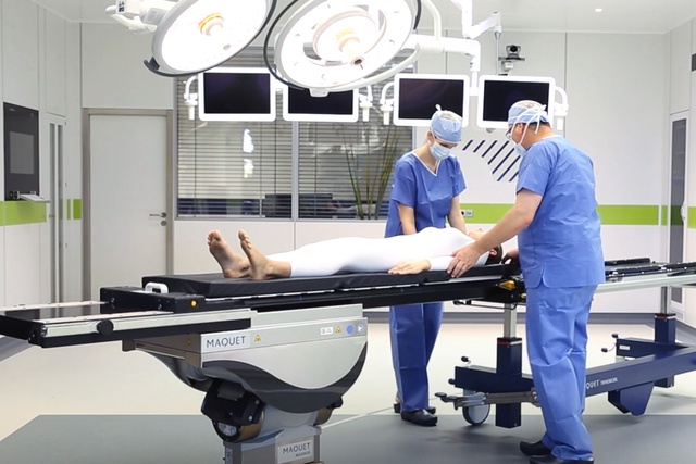 Deux professionnels de la santé en tenue d'hôpital ajustent un patient sur la table d'opération Maquet Magnus