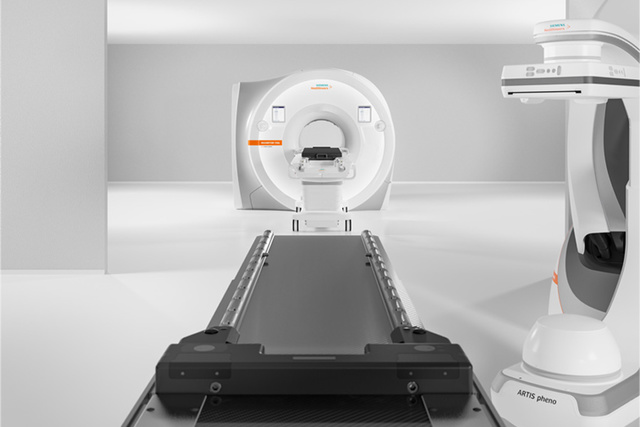 MRI machine in a bright, white medical room with a patient table and a nearby imaging device.