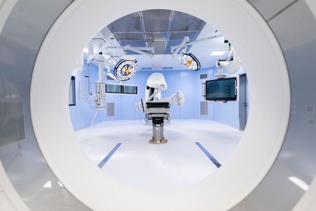 View through a circular scanner into a modern, sterile medical room with advanced equipment and monitors.