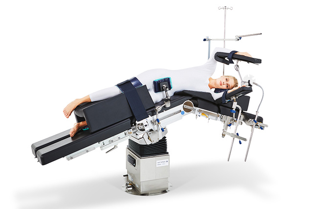 Eine Person liegt auf einem mechanischen Behandlungstisch, der geneigt und mit verschiedenen Stützen ausgestattet ist.